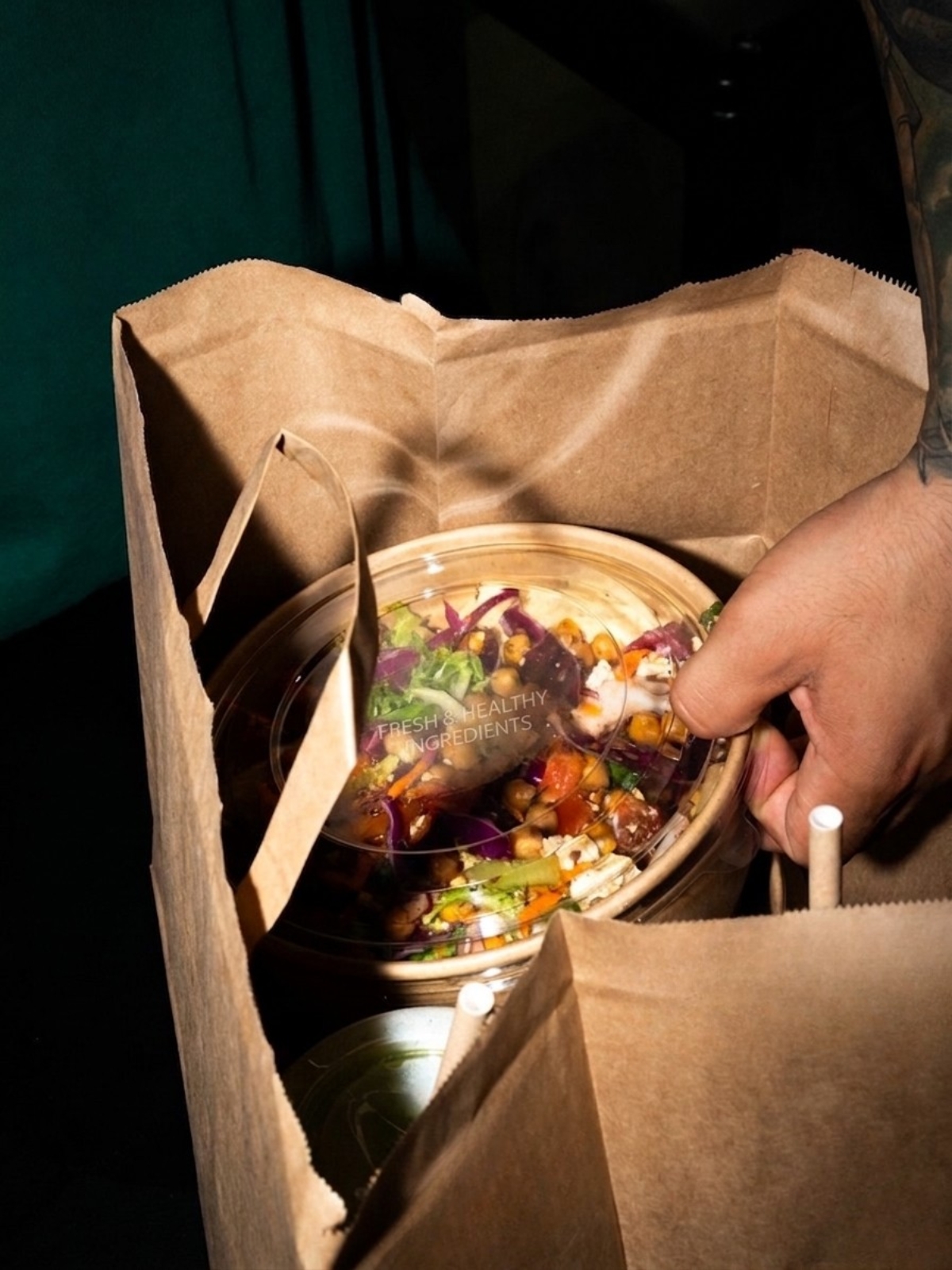 En person håller en takeaway-påse i papper med en hälsosam salladsskål som innehåller färska ingredienser